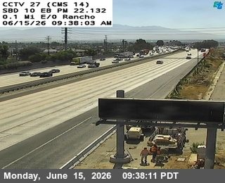 Two people are working on a truck with cones on the side of the road.