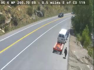 Tow truck with a trailer and van, person standing nearby on the roadside.