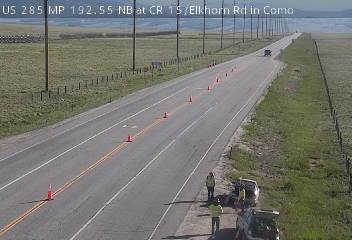 Two vehicles and personnel on the shoulder of the highway, with traffic cones present.