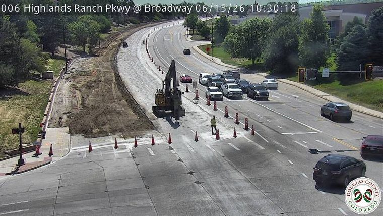 Construction zone with excavator and worker present, traffic cones and lane closures.