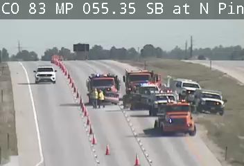 Emergency responders and vehicles are present on the roadway, directing traffic with cones.