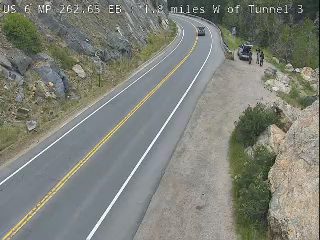 Two people and a vehicle are stopped on the shoulder of the road.