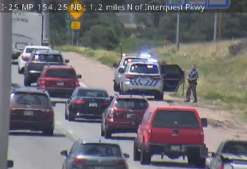 Police car with blue and red lights on the right shoulder with a person standing outside