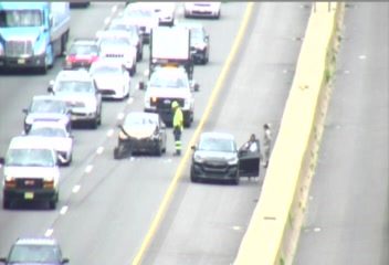 Two cars appear to be involved in a crash on the highway with people standing nearby.