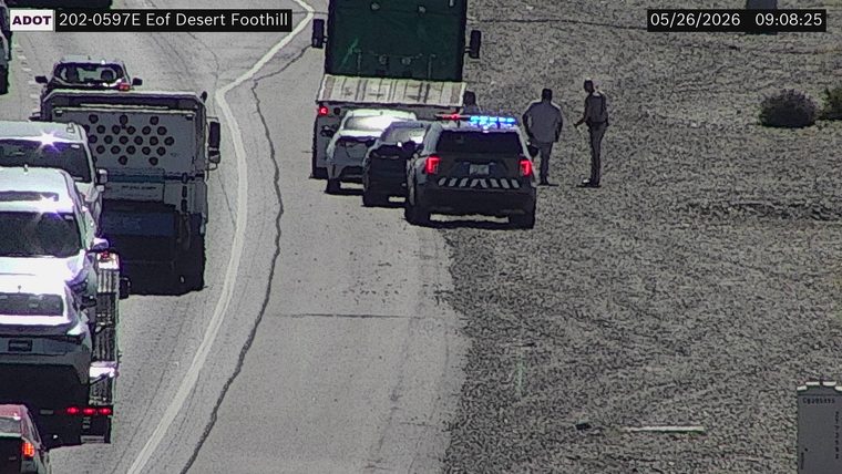 Police vehicle with flashing lights and people standing on the right shoulder