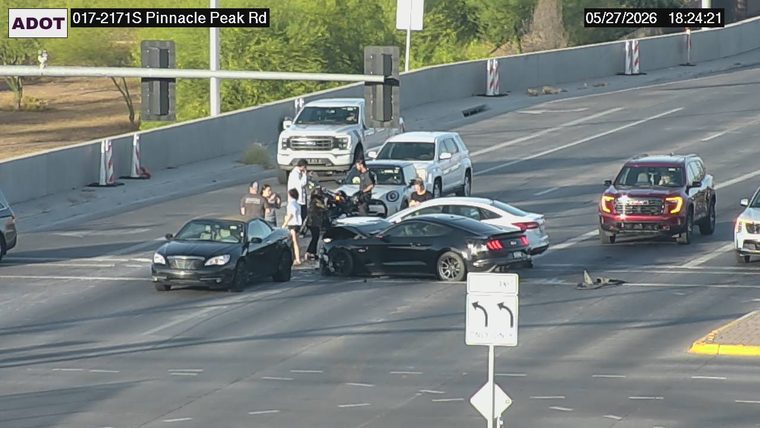 Multiple vehicles collided in the middle of the roadway with people standing outside and debris on the road