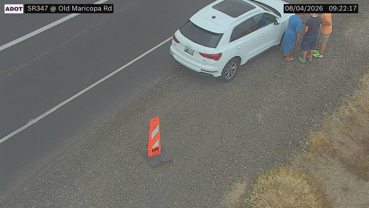 White SUV on the right shoulder with three people standing nearby