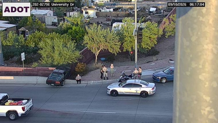 Black car off the roadway, partially on embankment, with several people standing nearby