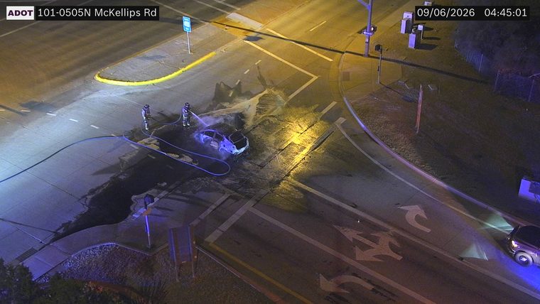 Two firefighters spraying water on a burning car in the intersection