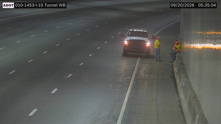 Two workers in high-visibility vests and hard hats near a service truck on the right shoulder
