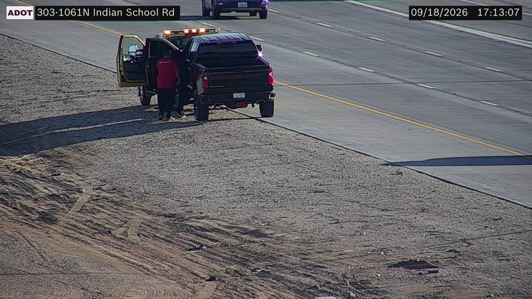 Yellow tow truck with hazard lights on assisting a black pickup truck on the right shoulder