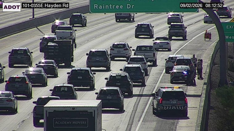 Police car with blue and red lights on the right shoulder with several people standing nearby