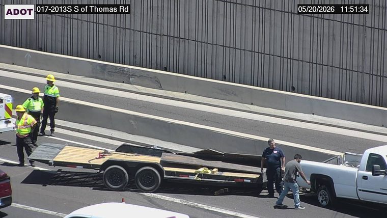 White pickup truck and flatbed trailer stopped on the shoulder with workers in safety vests and other people standing on the roadway