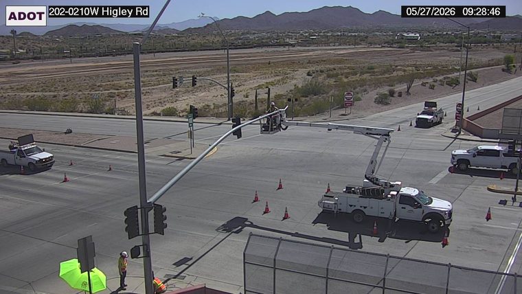 Utility truck with boom arm extended and worker in bucket working on traffic signal, surrounded by cones in the intersection