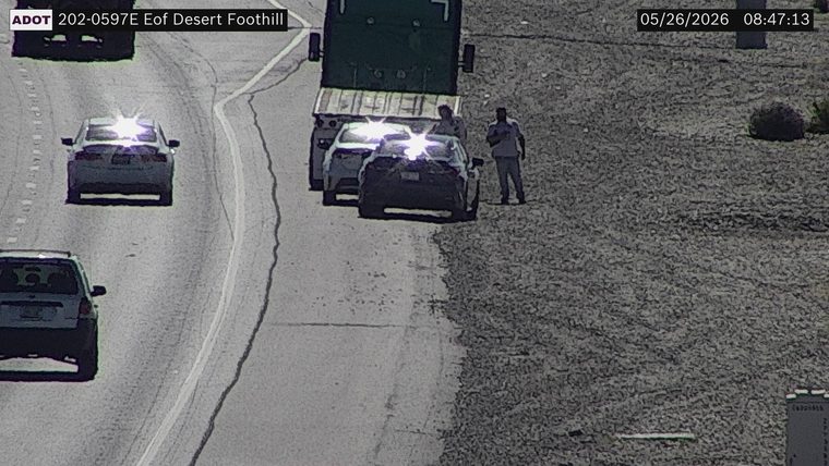 Two people standing on the right shoulder next to a truck and two cars stopped off the travel lanes