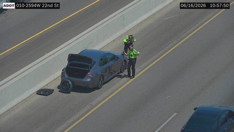 Two individuals in high-visibility vests attending to a car with its trunk open and a spare tire on the ground