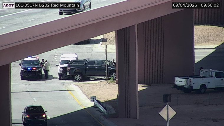 Police car with red and blue lights on the left shoulder, next to a damaged white van and a dark pickup truck