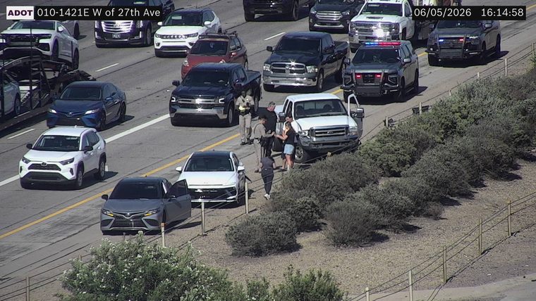 Two police officers interacting with individuals near a white pickup truck on the right shoulder