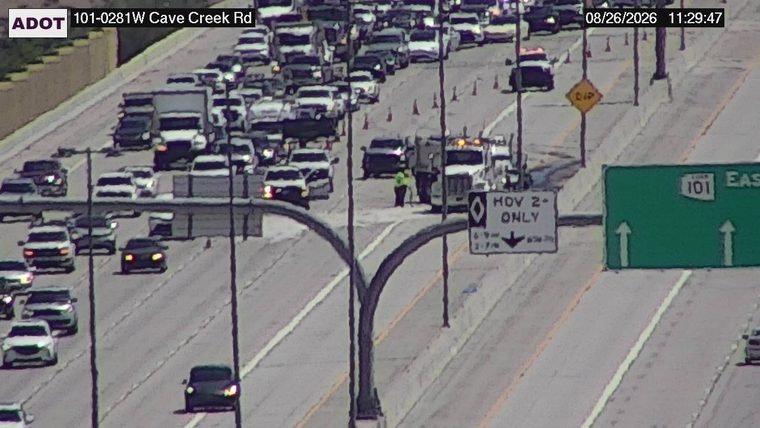 Two workers in high-visibility vests near a truck and traffic cones in the HOV lane
