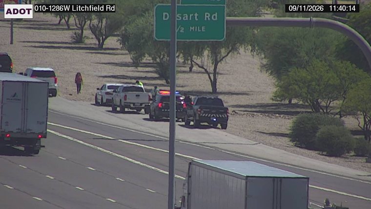 Two police cars with lights on and two civilians on the shoulder