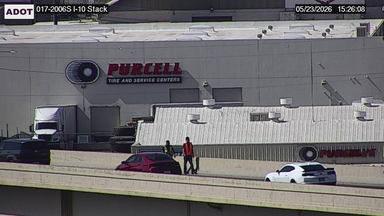 Two people in high-visibility vests standing on the roadway next to a red sedan