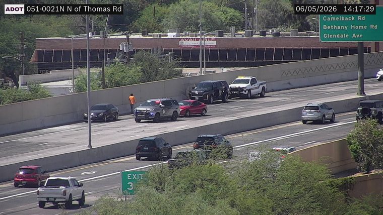 Police car with lights on and a person in an orange shirt near a red car in the left lane