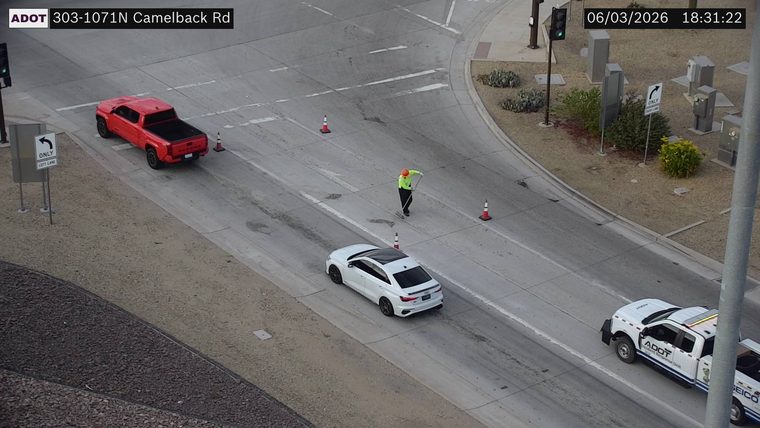 Worker with safety vest and orange helmet sweeping debris in the roadway with traffic cones present