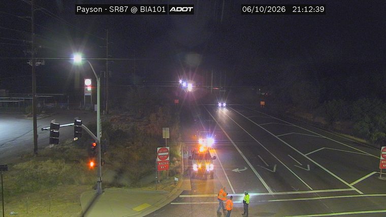 Three workers in the roadway near a vehicle with flashing lights