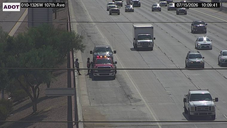 Tow truck with flashing amber lights and two individuals on the right shoulder