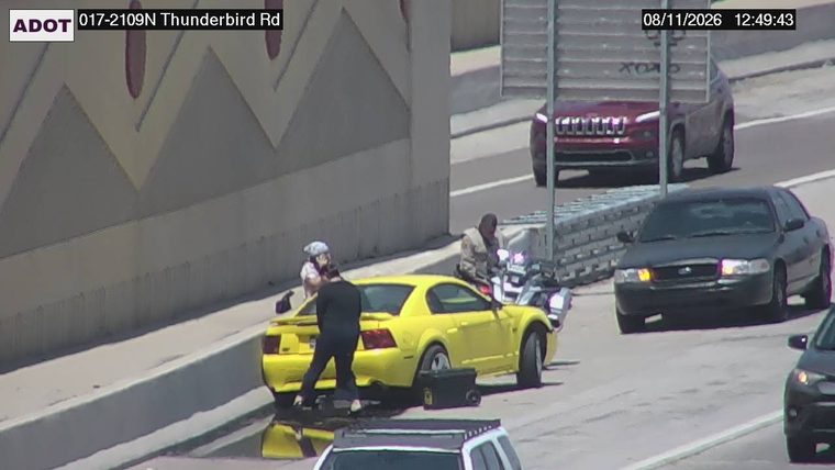 Two people interacting with a yellow car on the right shoulder, with a motorcycle nearby