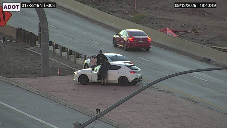 Three people gathered around a white car on the right shoulder
