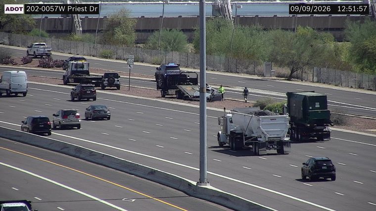 Tow truck with a damaged car on its flatbed, and a police vehicle with lights on, on the right shoulder