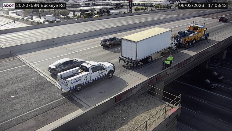 Two people and a tow truck attending to a white box truck on the right shoulder
