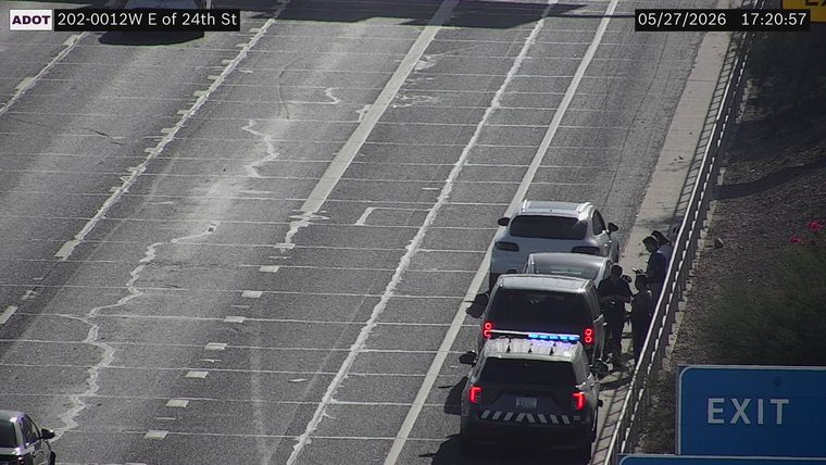 Police vehicle with flashing blue lights and multiple stopped vehicles with people standing on the right shoulder