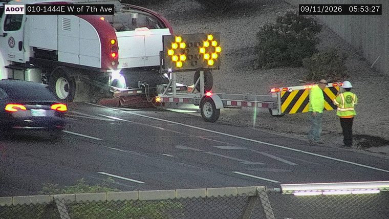 Two workers in high-visibility vests near a trailer with an arrow board and traffic control devices
