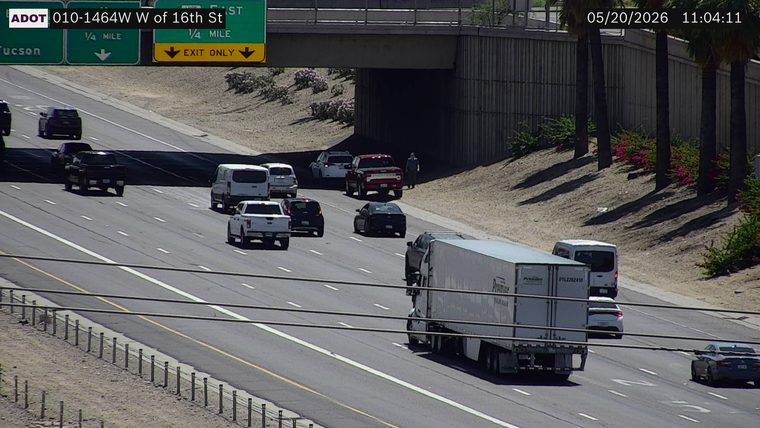 Pedestrian standing on the right shoulder next to a red pickup truck under the overpass