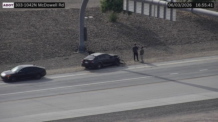 Black sedan with visible front-end damage on the right shoulder with two people standing nearby