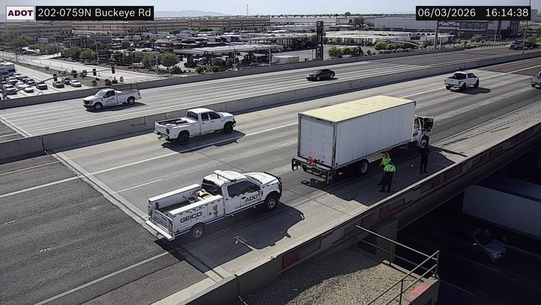 Two individuals standing near a white box truck in the right lane