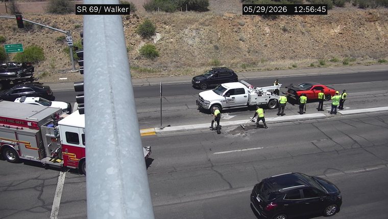 Red sports car with front-end damage and a tow truck with several people around it in the right lane