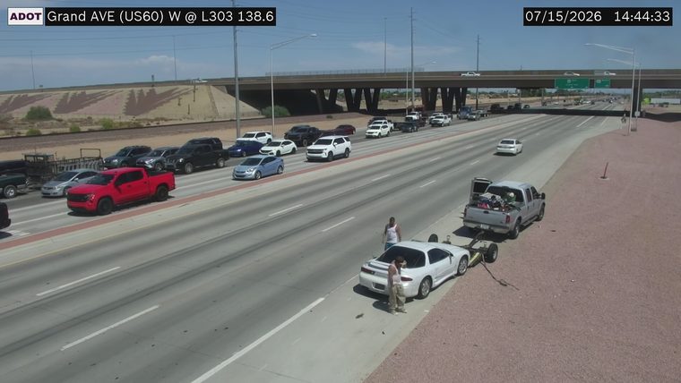 Two people standing next to a white car being towed by a pickup truck on the right shoulder