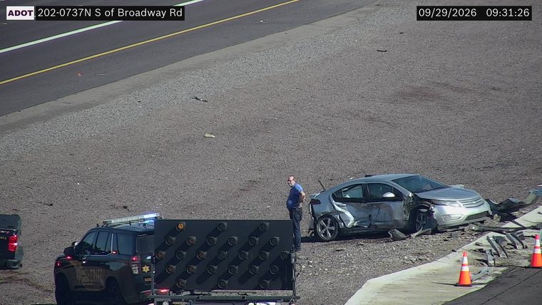 Silver sedan with significant collision damage off the travel lanes, with a sheriff's vehicle and a traffic control board present