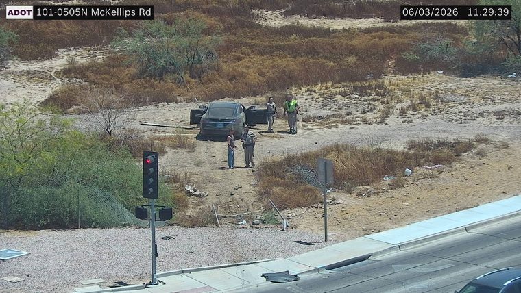 Two individuals and two persons in uniform standing near a car with doors open off the roadway