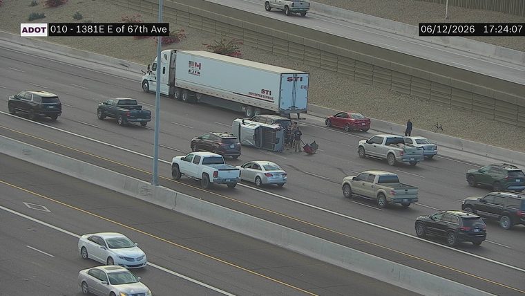 Overturned vehicle with people around it in the middle lanes