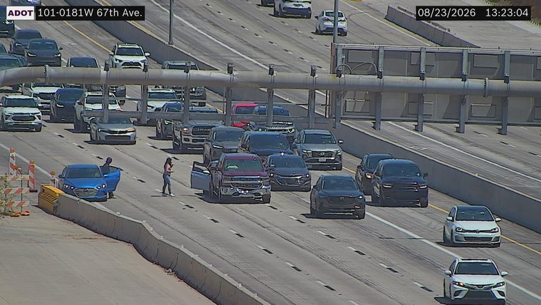 Two people standing outside a blue sedan in the left lane