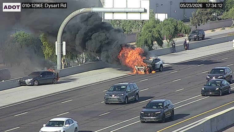 White SUV on fire on the left shoulder with heavy flames and thick black smoke