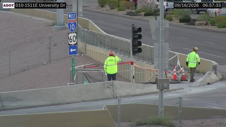 Two workers in high-visibility vests near traffic cones and construction barriers