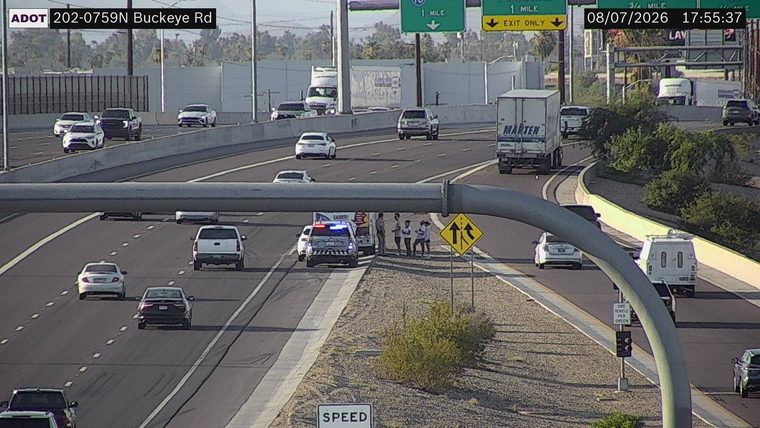 Police car with lights on in the left lane with several people standing nearby