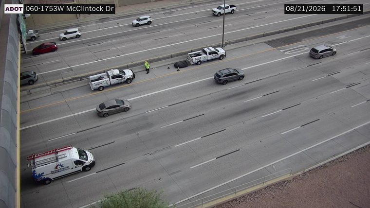 Two ADOT trucks and a worker on the right shoulder with a large black object on the roadway