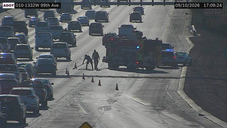 Fire truck with red and blue lights on, two workers on the roadway, and traffic cones