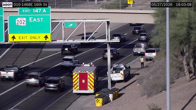 Fire truck, ADOT Incident Response Unit, and police vehicle with flashing lights on the right shoulder and lanes, with a responder on foot near a vehicle on the shoulder